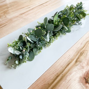 Puede incluir: Una guirnalda de eucalipto verde y blanca con peque&ntilde;as flores rosas, ideal para decorar una mesa o una repisa de la chimenea.
