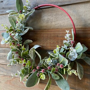 May include: A red metal wreath with frosted eucalyptus leaves and red berries.