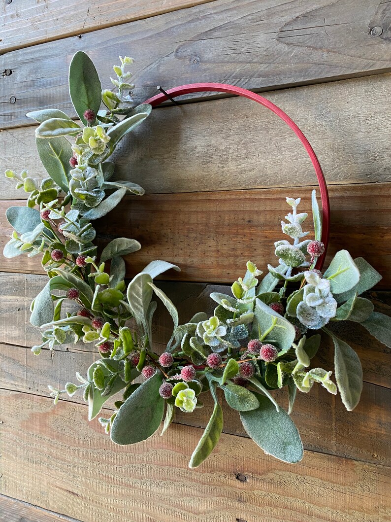 May include: A red metal wreath with frosted eucalyptus leaves and red berries.