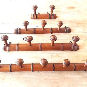 May include: Four wooden coat racks made of bamboo with round wooden knobs. The racks are stacked on top of each other, with the top rack having two knobs, the second rack having three knobs, the third rack having five knobs, and the bottom rack having five knobs.