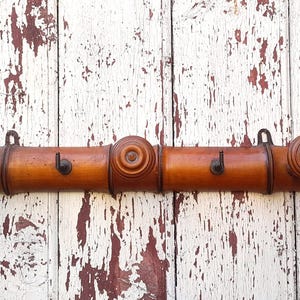 May include: A wooden coat rack with three hooks. The rack is made of three sections of brown wood with rounded ends. The hooks are made of metal and are attached to the wood.