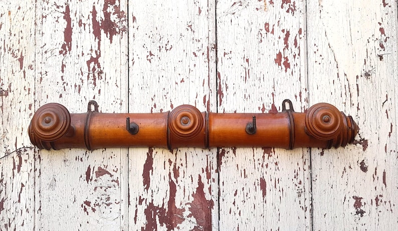 May include: A wooden coat rack with three hooks. The rack is made of three sections of brown wood with rounded ends. The hooks are made of metal and are attached to the wood.