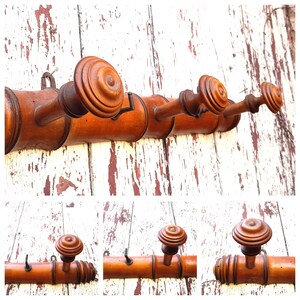 May include: A wooden coat rack with five hooks. The rack is made of brown wood and has a natural finish. The hooks are made of metal and have a black finish.