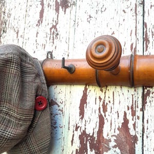 May include: A wooden coat rack with a brown knob and a brown and white plaid hat hanging on it.
