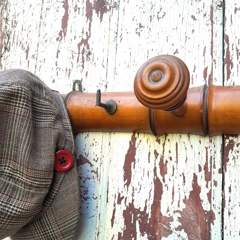 May include: A wooden coat rack with a brown knob and a brown and white plaid hat hanging on it.