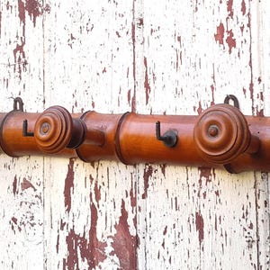 May include: A wooden coat rack with three hooks. The rack is made of dark brown wood and has a decorative design. The hooks are made of metal and are painted black.