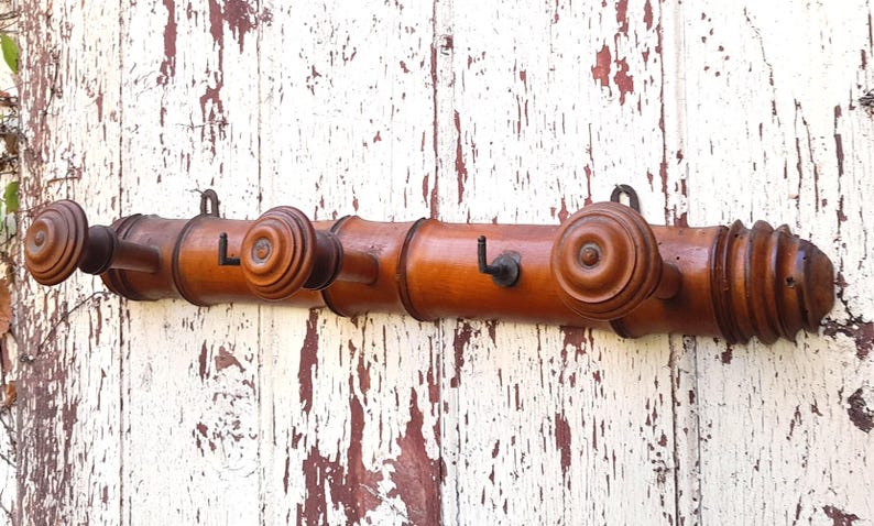 May include: A wooden coat rack with three hooks. The rack is made of dark brown wood and has a decorative design. The hooks are made of metal and are painted black.