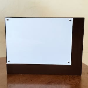 May include: A brown wooden picture frame with a white acrylic insert. The frame has a small lip around the edge of the insert.