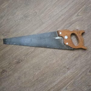 May include: A hand saw with a wooden handle and a metal blade. The blade is gray and has teeth along one edge. The handle is made of light brown wood and is attached to the blade with two rivets.