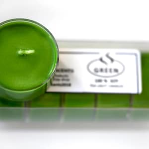 May include: A close-up of a green tea scented candle in a clear glass container. The candle is part of a set of six candles, all in a clear plastic box with the label "GREEN" printed on it.