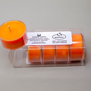 May include: A package of six orange soy wax tea light candles with the label "WASSAIL 100% SOY SCENTED TEA LIGHT CANDLES" and "PHOENIX SCENTS" with a list of scents: Orange Peel, Cinnamon, Lemon, Apple Cider, Red Currant, Cranberry Wood, Red Wine, Cedarwood. Find us on ETSY PhoenixScents2018.