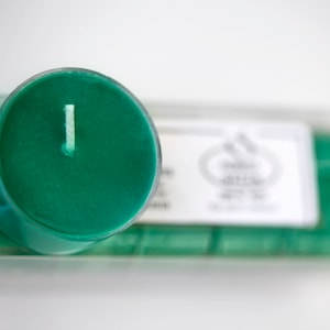 May include: A green tea scented candle in a clear glass jar with a white wick. The candle is packaged in a clear plastic box with a white label that says "Green Tea" and "Scented Candle".