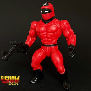 May include: A red action figure with a black skull and crossbones on its head, holding a black gun. The figure is wearing a red suit with a black belt and black boots.