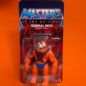 Puede incluir: Figura de acción de General Enos de Masters of the Universe, versión Beastman. La figura es naranja y azul con una máscara facial con forma de cráneo. La figura está empaquetada en una tarjeta con el logotipo de Masters of the Universe.