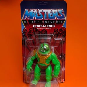 Può includere: Una action figure verde di General Enos, una versione Moss Man, di Masters of the Universe, in una confezione di plastica con sfondo rosso e nero.