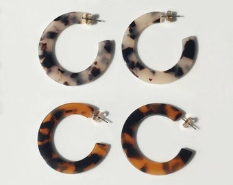 May include: Four pairs of hoop earrings in the image. Two pairs have a speckled pattern in shades of cream, brown, and black. The other two pairs have a tortoiseshell pattern in shades of brown and black. All earrings have gold-colored posts.