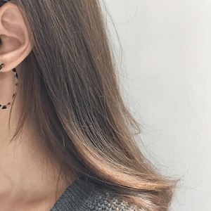 May include: Large hoop earrings with a tortoiseshell pattern in shades of brown, black, and cream. The earrings are circular and worn on the ear. The image shows a close-up of the earrings and part of the person's face.