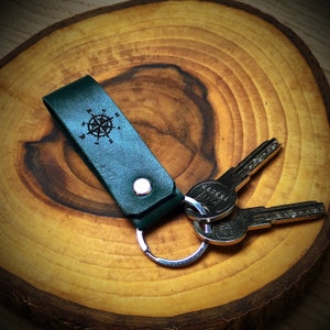 May include: A dark green leather keychain with a compass design and a silver key ring. Two silver keys are attached to the ring.