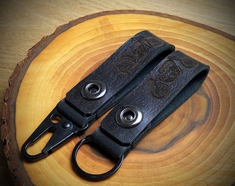 May include: Two black leather keychains with metal rings and snap closures. Each keychain features an engraved motorcycle design.