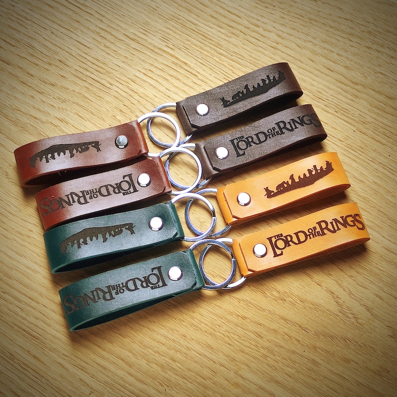 May include: Six leather keychains with silver key rings. Each keychain features a different design with the words "The Lord of the Rings" and a silhouette of a scene from the movie.
