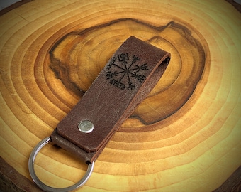 May include: A brown leather keychain with a silver key ring. The leather has a design of a compass with a star in the center.