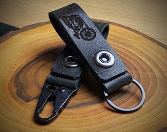 May include: Black leather key chain with a motorcycle design and a metal ring. The keychain has two snap closures.
