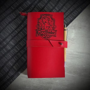 Op de afbeelding: Rood leren dagboek met een Gryffindor-huiswapen en een houten pen die aan de omslag is bevestigd.