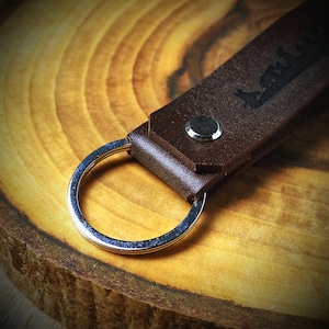 May include: A brown leather keychain with a silver key ring. The leather has a design embossed into it.