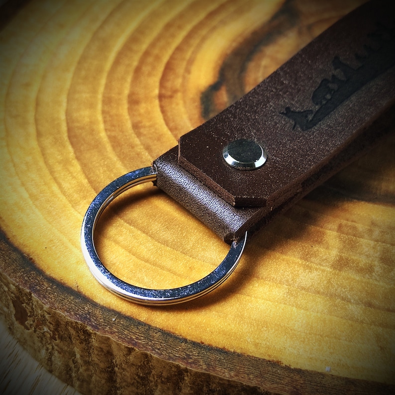 May include: A brown leather keychain with a silver key ring. The leather has a design embossed into it.