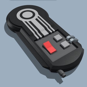 May include: A black and gray rectangular device with a red switch, two gray buttons, and a series of parallel lines. The device has a rounded top with a circular design and a small cylindrical component on the side.