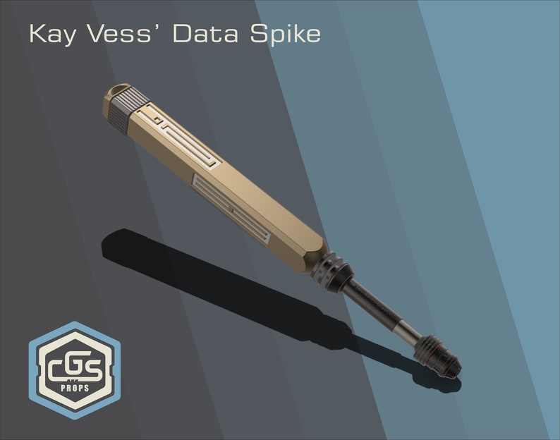 Puede incluir: Un accesorio de punta de datos dorado y negro, con las palabras "Kay Vess' Data Spike" en el fondo. El accesorio es una r&eacute;plica de un dispositivo ficticio de una serie de televisi&oacute;n de ciencia ficci&oacute;n.