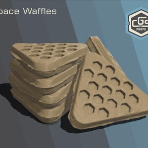 May include: A stack of tan, triangular waffles with a honeycomb pattern, labeled "Space Waffles." The waffles are stacked on top of each other, with one waffle leaning against the stack. The background is a gradient of gray and blue.