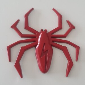 May include: A red plastic spider with a lightning bolt design on its body. The spider has eight legs and is a decorative item.