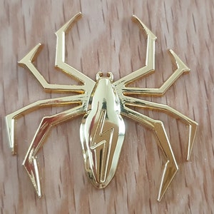 May include: A gold-colored metal spider with a lightning bolt design on its body. The spider has eight legs and is a decorative piece.