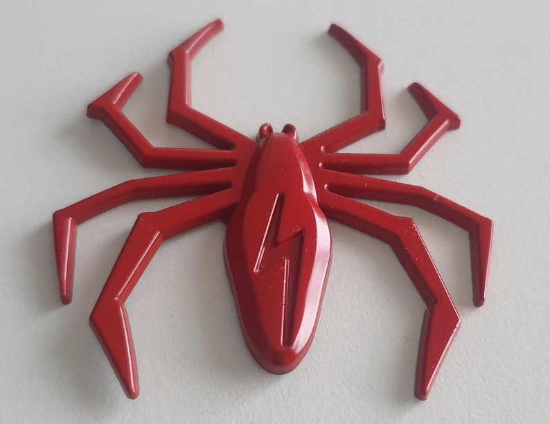 May include: A red plastic spider with a lightning bolt design on its body. The spider has eight legs and is a decorative item.