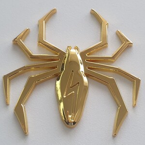 May include: A gold-colored metal spider with a lightning bolt design on its body.