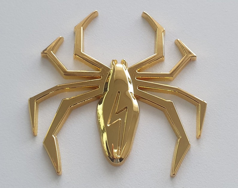 May include: A gold-colored metal spider with a lightning bolt design on its body.