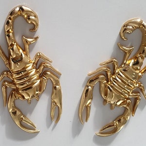 May include: Two gold-coloured scorpion figurines. The scorpions are facing opposite directions and have detailed carvings.