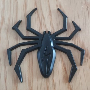 May include: Black plastic spider with eight legs and a lightning bolt design on its body.