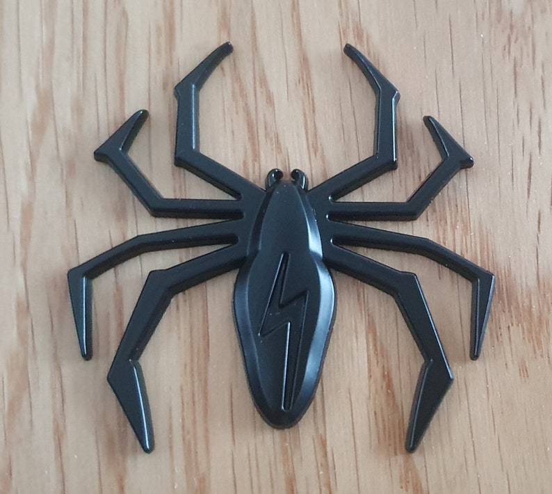 May include: Black plastic spider with eight legs and a lightning bolt design on its body.