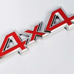 Peut inclure: Un emblème 4x4 rouge et argent. L'emblème est en métal et présente un design en relief.