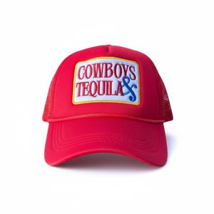 May include: A red trucker hat with a mesh back and a curved peak. The front panel displays a rectangular patch with the words "COWBOYS TEQUILA" in white and blue lettering, outlined in yellow.