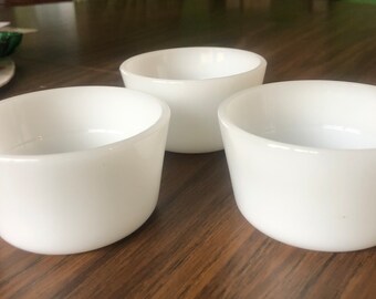May include: Three white ceramic bowls, each with a smooth, rounded rim. The bowls are arranged in a triangular pattern on a wooden surface.