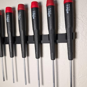 May include: A set of eight red and black screwdrivers with the brand name "wiha" printed on the handles. The screwdrivers are mounted on a black magnetic strip.