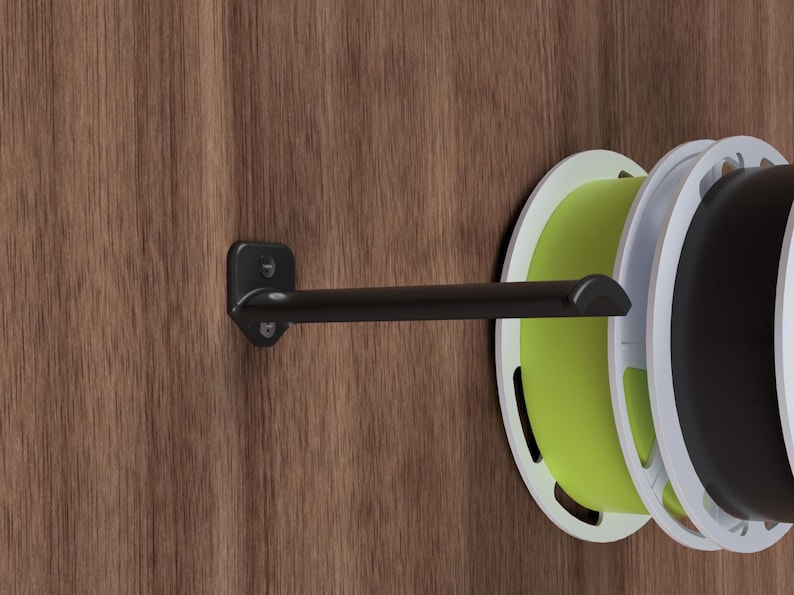 May include: A black metal wall-mounted spool holder with a single spool of green filament attached. The holder is mounted on a wood panel.