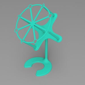 May include: A teal-colored, 3D-printed object with a circular, wheel-like top and a curved base. The wheel has spokes and small circular openings. The object stands upright on a U-shaped base, connected by a vertical stem.