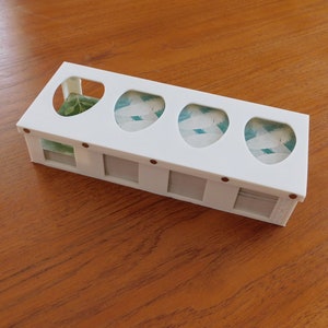 以下が含まれることがあります： 5つの区画があり、各区画に透明な窓が付いた白いプラスチック製の収納ボックス。窓には緑と白の葉の模様が見える。