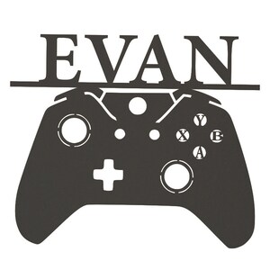 Pode incluir: Silhueta preta de metal de um controlador de videogame com o nome "EVAN" acima.