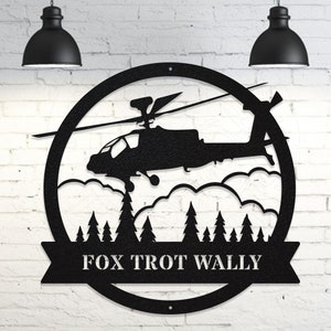 May include: Black metal wall art featuring a silhouette of a helicopter flying over a forest with clouds. The text "FOX TROT WALLY" is displayed on a banner below the helicopter.