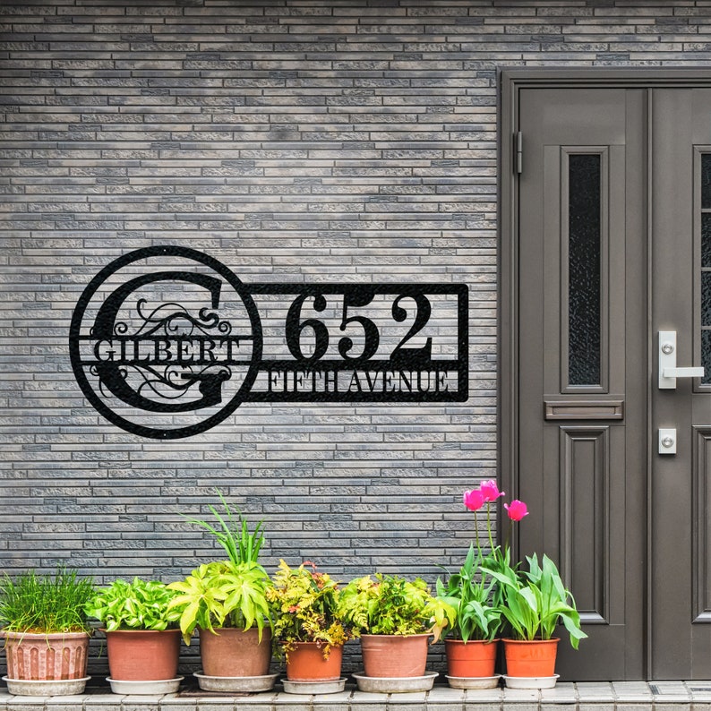 May include: Black metal house number sign with a circle featuring the letter G and the word "GILBERT" and a rectangular sign with the number "652" and the words "FIFTH AVENUE".